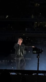 Ваня Дмитриенко выступает в полном росте перед толпой в темном освещении; видна сцена, прожекторы и масштаб концерта в «Лужниках».