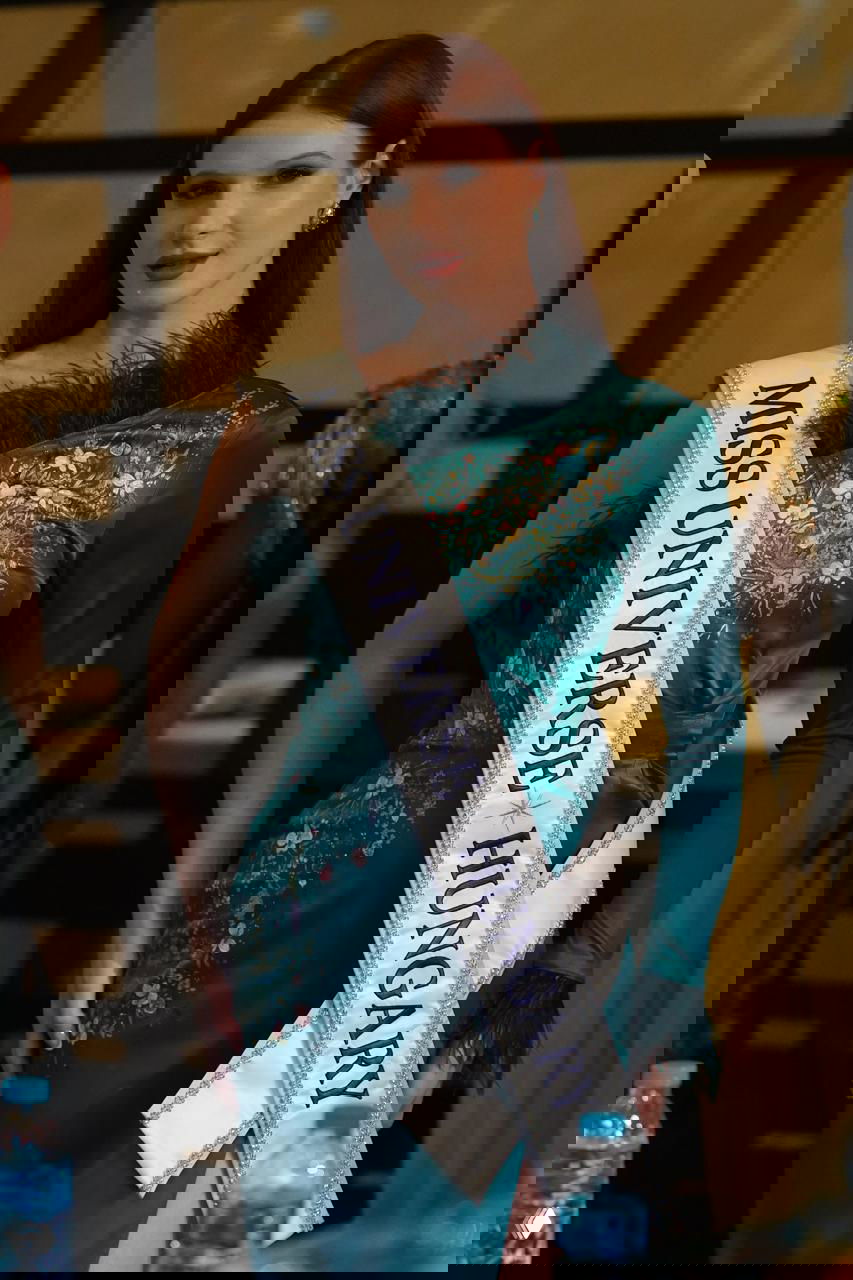 Портрет участницы с лентой «MISS UNIVERSE HUNGARY» в бирюзовом платье с вышивкой, снимок сделан внутри конференц-зала