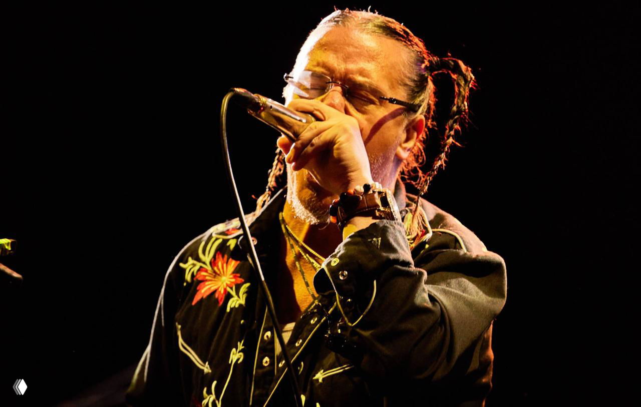 Крупный план вокалиста на сцене с микрофоном в руках: эмоциональное исполнение, тёплое сценическое освещение и сценический образ.