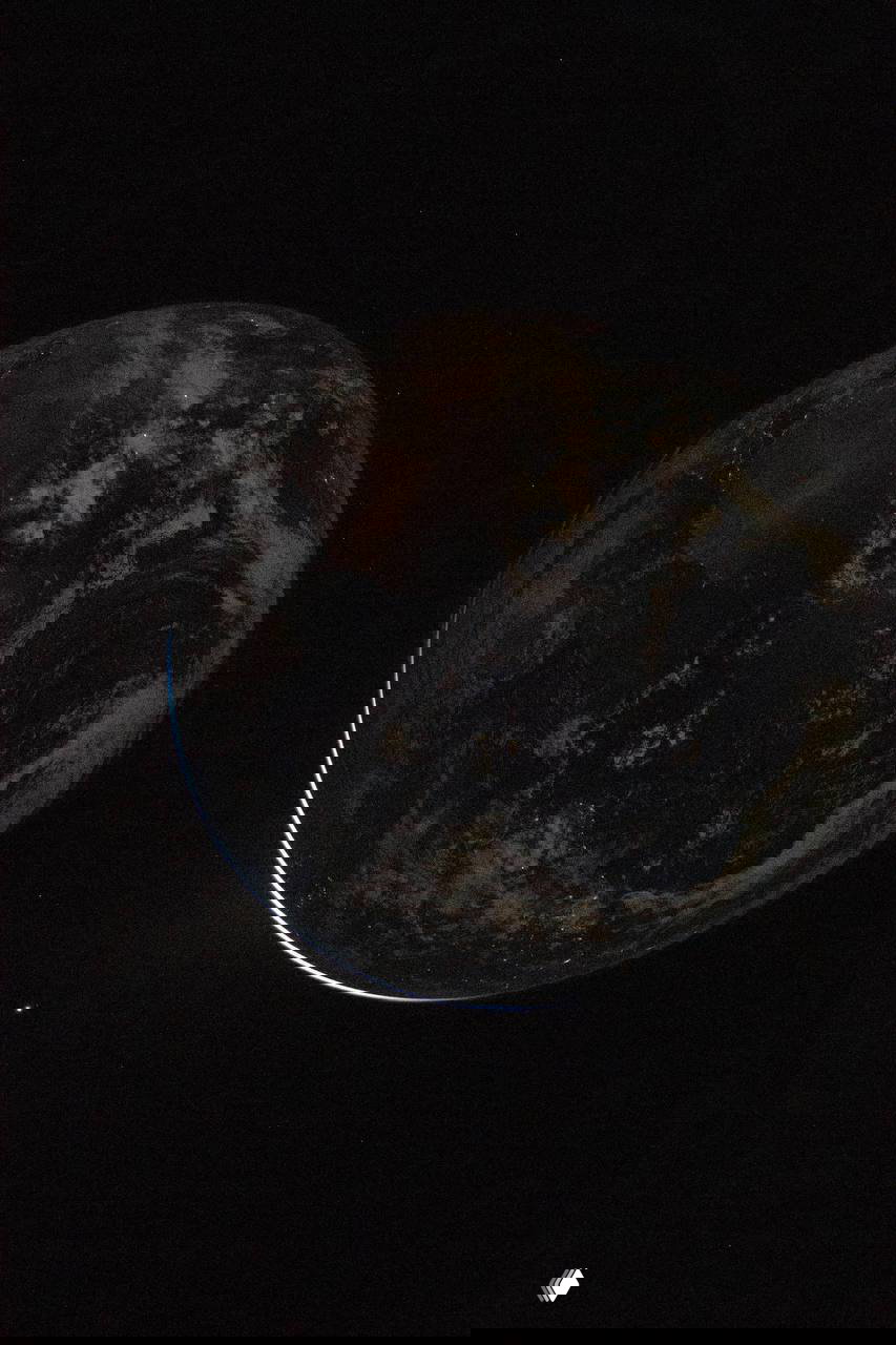 Контрастный кадр Земли в космосе: тонкая светящаяся кромка планеты, тёмная ночная сторона и слабые очертания материков.