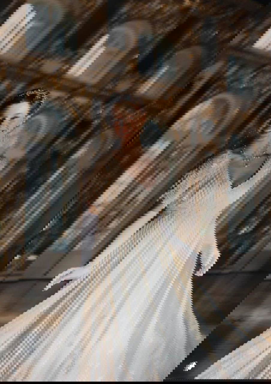 Полина Гухман в длинном белом платье, идёт по залу дворца с позолоченной лепниной и большими окнами — крупный план костюмной работы.