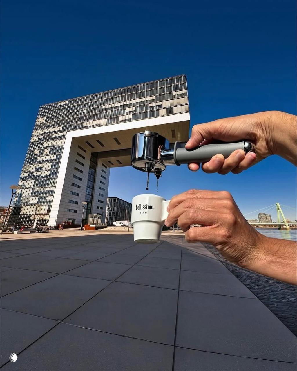 Две руки с портафильтром и мини-чашкой: кажется, что кофе льётся прямо из здания в чашку — забавная игра перспективы.