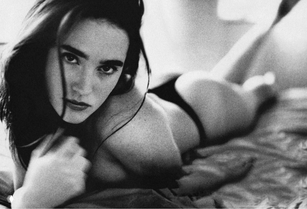 Лежащая в белье женщина на кровати, чёрно‑белый ретро‑кадр с интимной позой и контрастной плёночной зернистостью.