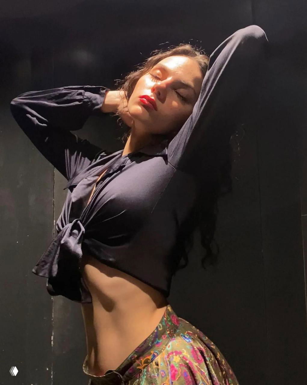 Артистичная студийная фотография: женщина в тёмной блузе, руки за головой, контрастный свет, подчёркнутый профиль и силуэт.