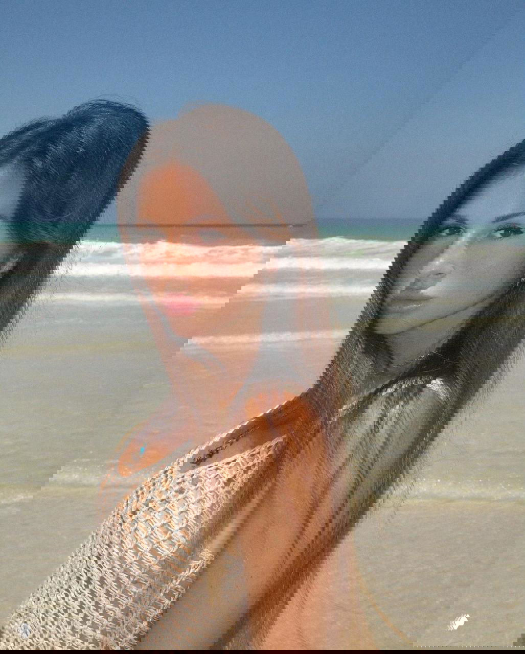 Портрет женщины на пляже с морским фоном, летняя съемка в натуральном образе — акцент на лице, коже и спокойной позе.