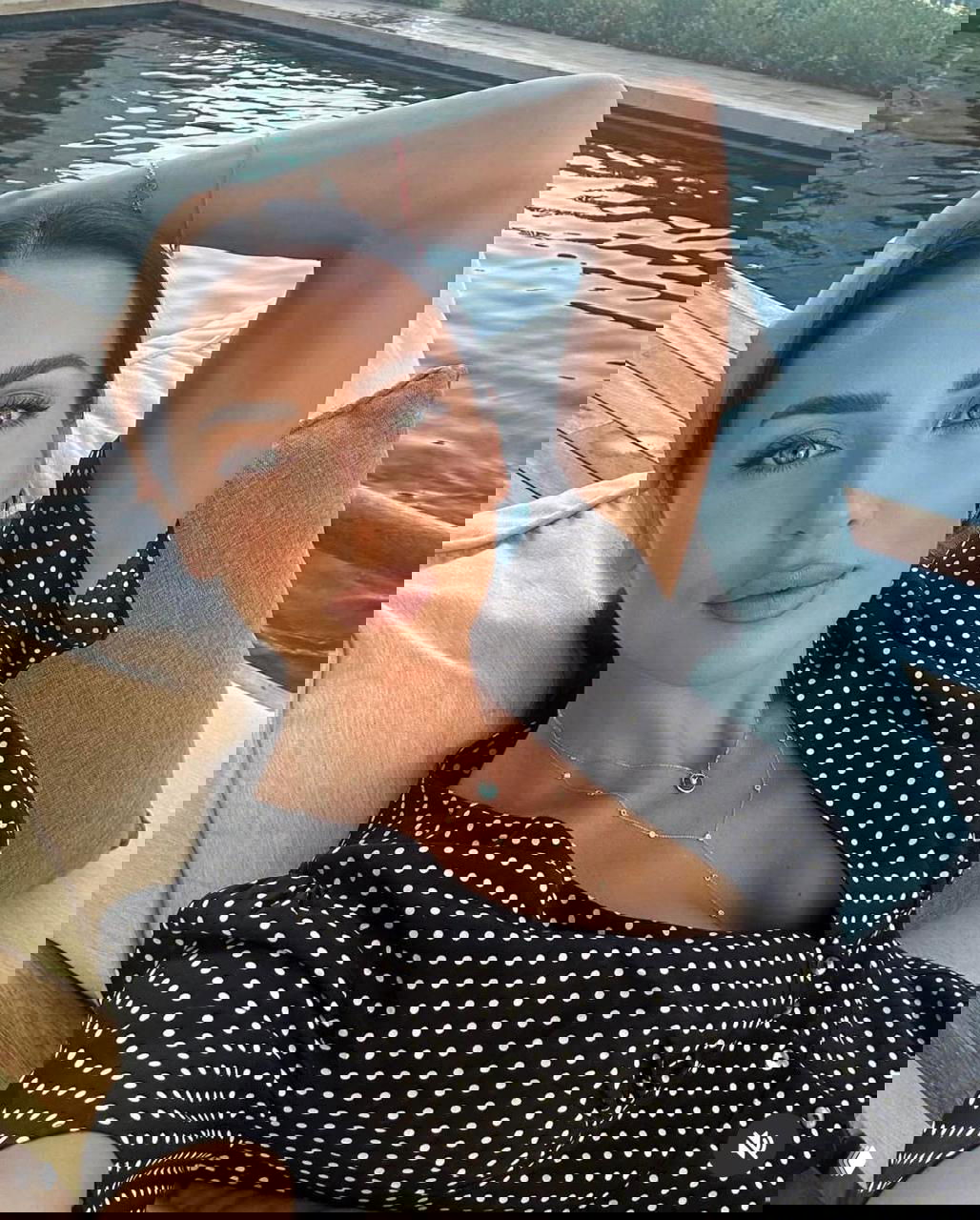 Селфи женщины у бассейна крупным планом в черном в горошек наряде, расслабленная поза, украшения и акцент на лицевом выражении.