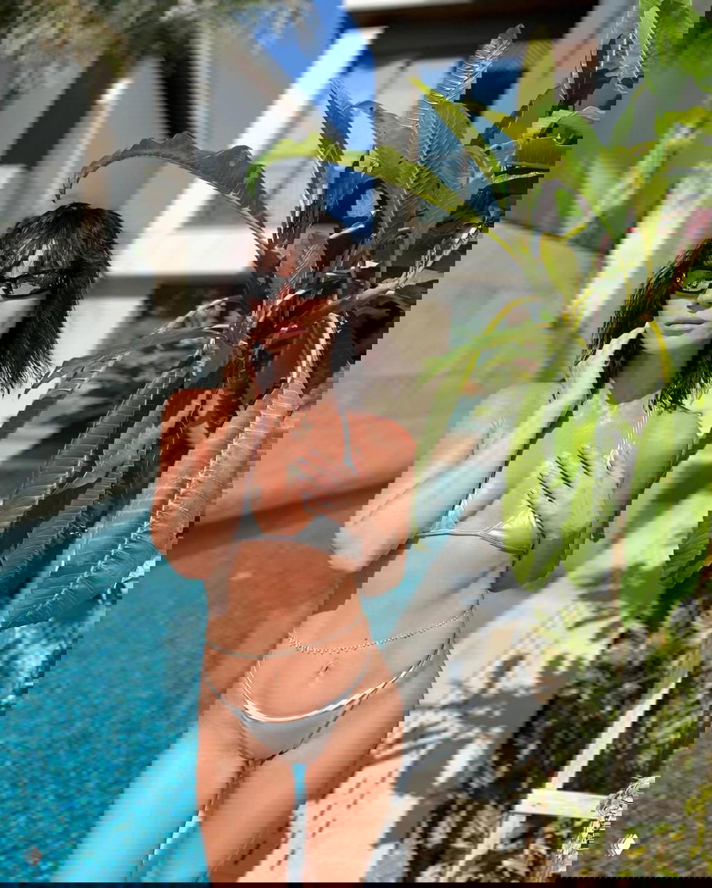 Женщина в серебристом бикини у бассейна в полный рост, на фоне тропических растений и современной виллы — солнечная уличная фотосессия.