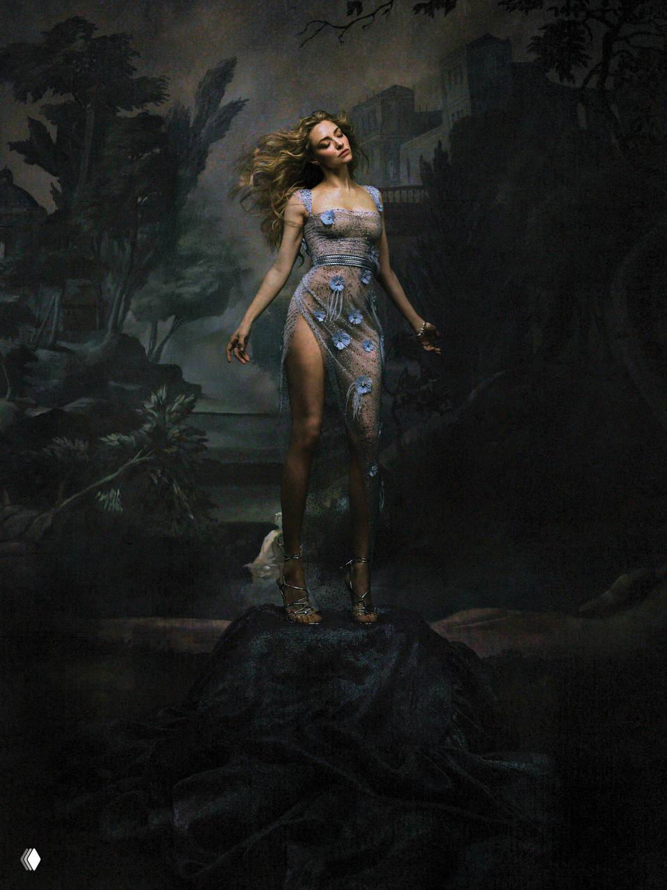 Полноформатный студийный кадр: женщина в полупрозрачном платье с цветочными элементами на тёмном художественном фоне создаёт театральный, романтичный образ.