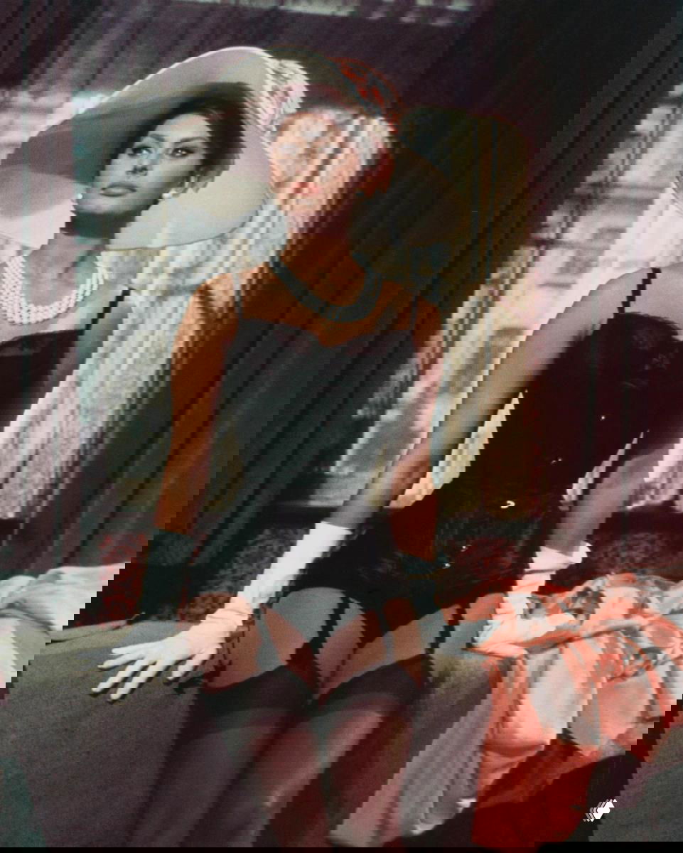 Женщина в ретро-костюме и широкополой шляпе, постановочная сцена из фильма с корсетом и чулками, театральная поза.