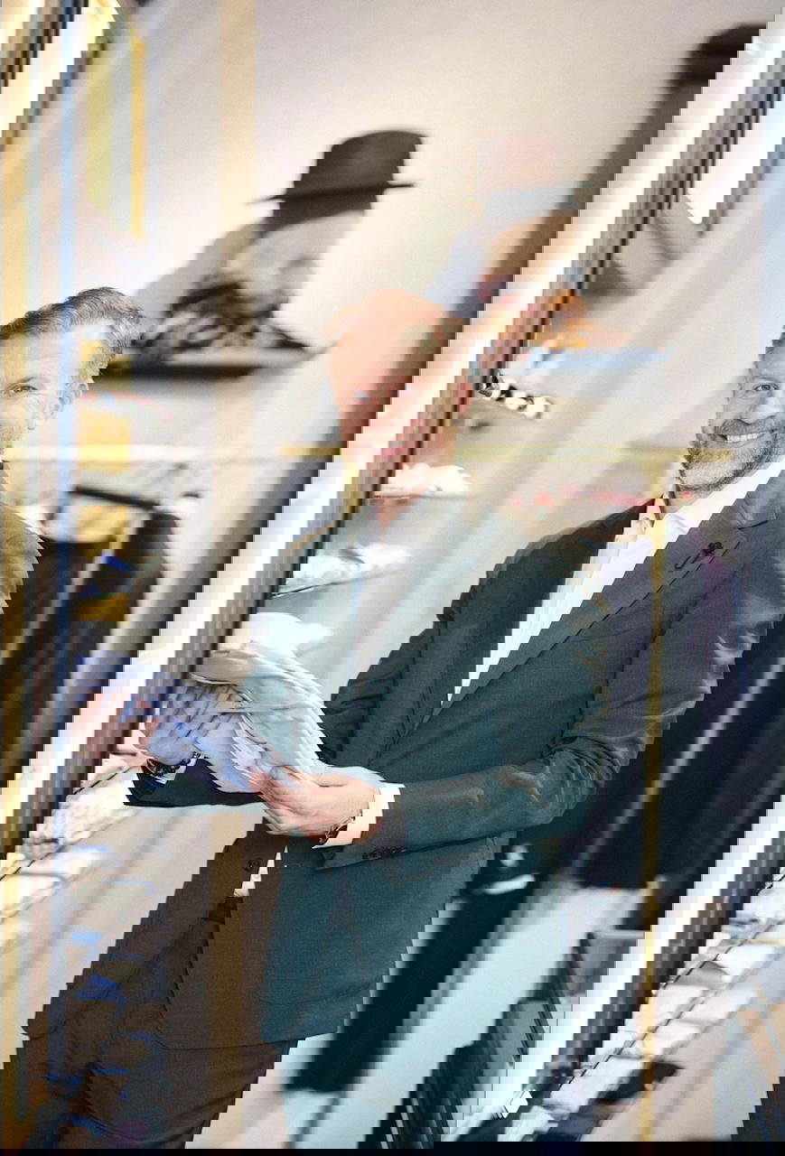 Николай Демин в магазине одежды среди рубашек и костюмов; держит рубашку в руках и улыбается, репортажный кадр из проекта.