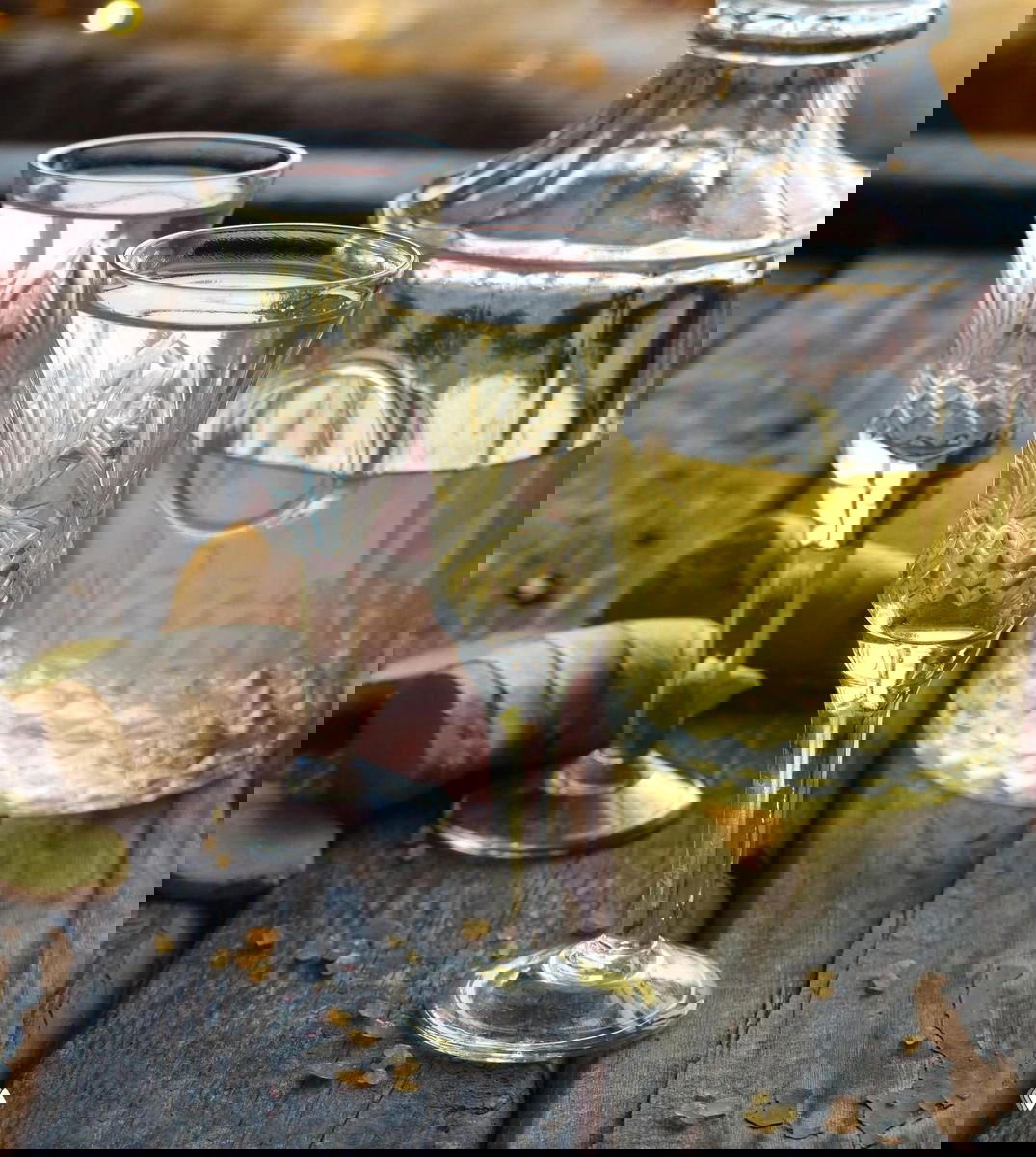 Хрустальные рюмки и графин со светлой настойкой на деревянной поверхности; рядом кусочки имбиря и кристаллы сахара.