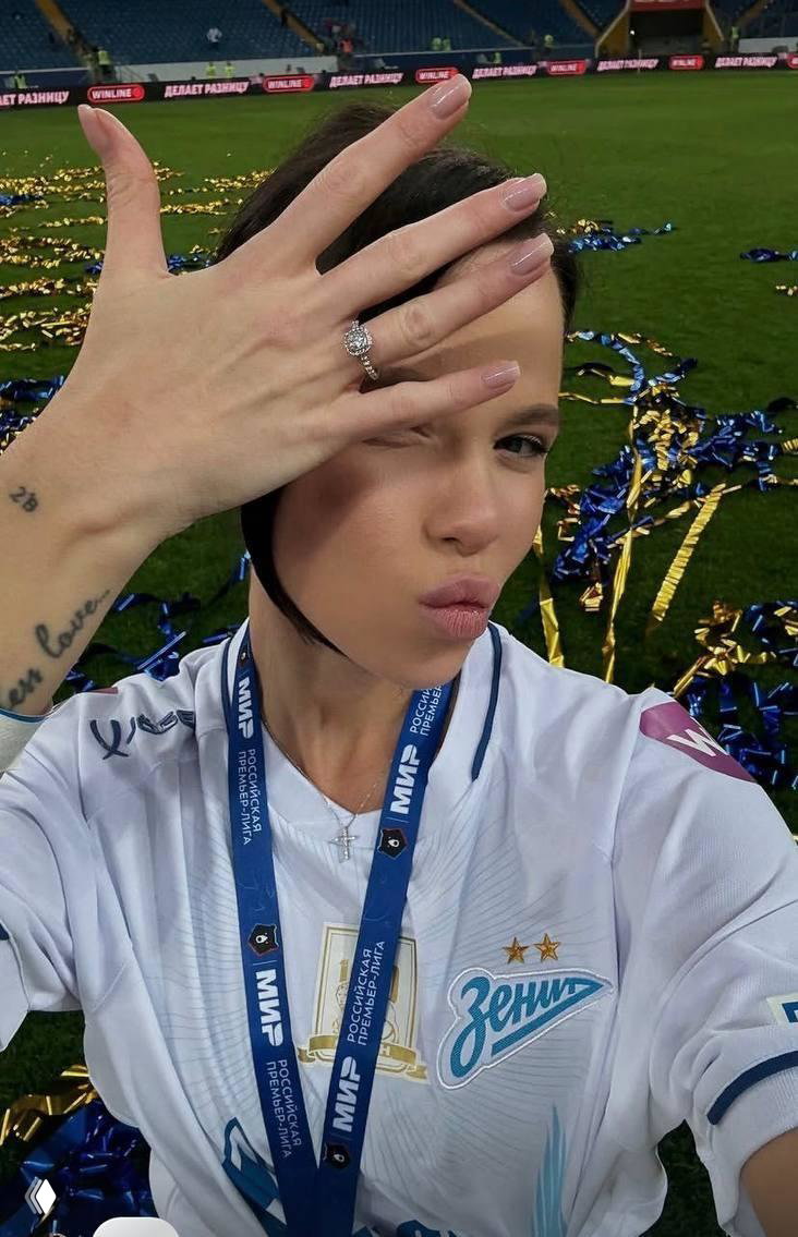Крупный план руки девушки с обручальным кольцом на фоне газона и праздничных украшений стадиона — демонстрация помолвочного/свадебного кольца.