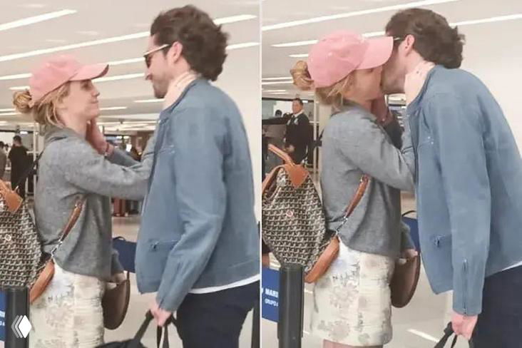 Две фигуры в повседневной одежде целуются в зале ожидания аэропорта; видны сумки, прохожие и обычная бытовая обстановка, съёмка папарацци.