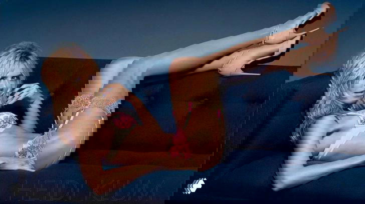 Модель в корсетном белье и чулках позирует на диване в гламурной студийной съёмке, акцент на позе, образе и ногах.