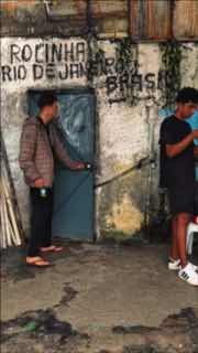 Детальный кадр: двое мужчин у двери фавел, потрескавшиеся стены и уличный фон Рио, без фокусировки на лицах.