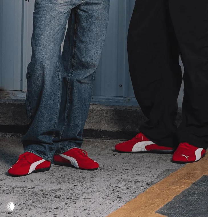 Низ кадра: ноги в широких джинсах и парах красных «торпедных» кроссовок, видны только обувь и штанины.
