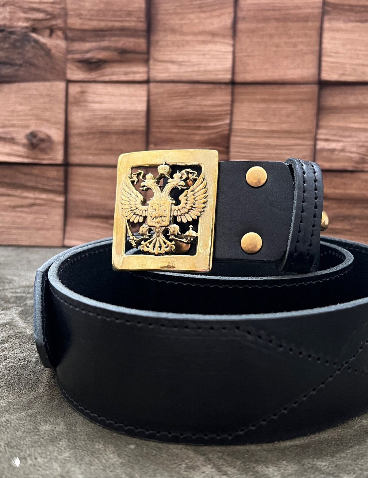 Черный ремень в спирали; на бронзовой пряжке — двуглавый орел, крупный план, акцент на деталях и патине металла.