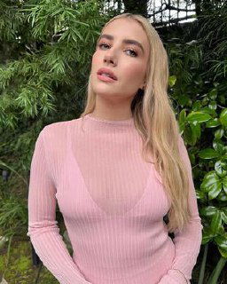 Натуральный портрет блондинки в розовом свитере на фоне зелени, мягкое освещение, акцент на лице и casual-стиле.