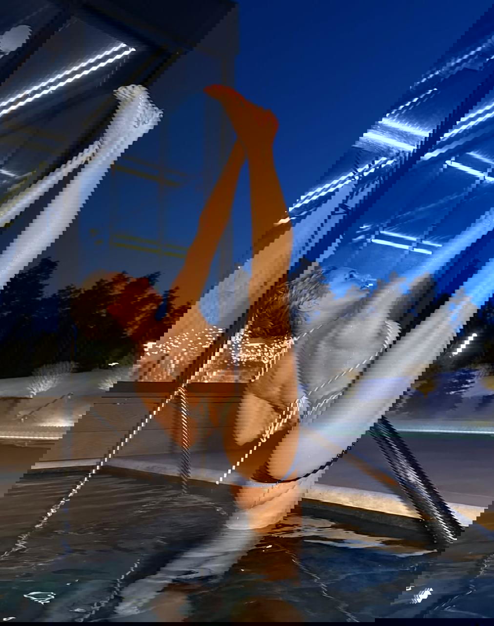 Виктория Цуранова выполняет растяжку в бассейне в бикини, подчёркивая сильный пресс и гибкую осанку на фоне леса.