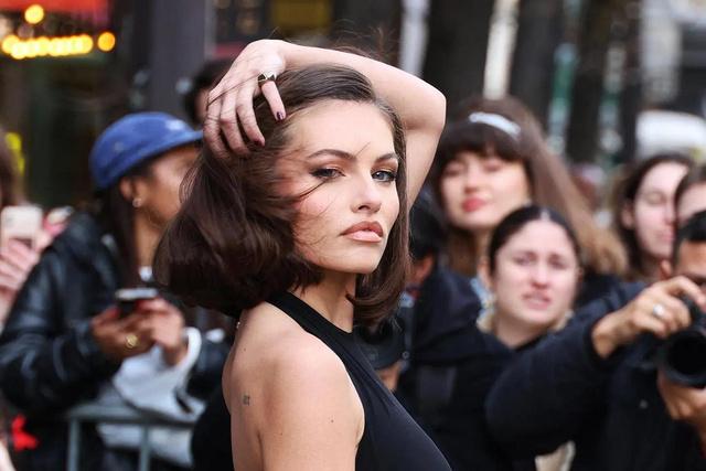 Тилан Блондо на уличном мероприятии среди зрителей: винтажный образ, тёмный макияж, взаимодействие с публикой и папарацци на заднем плане.