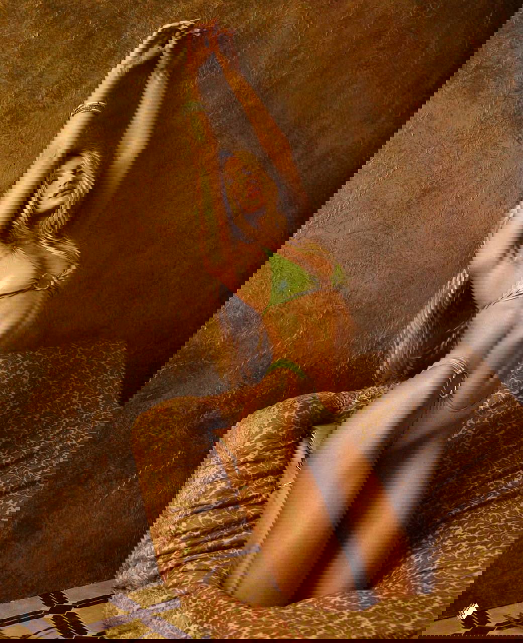 Женщина-модель в зелёном бикини стоит с поднятыми руками на фоне золотистых стен и бархатного кресла — кадр кампании.