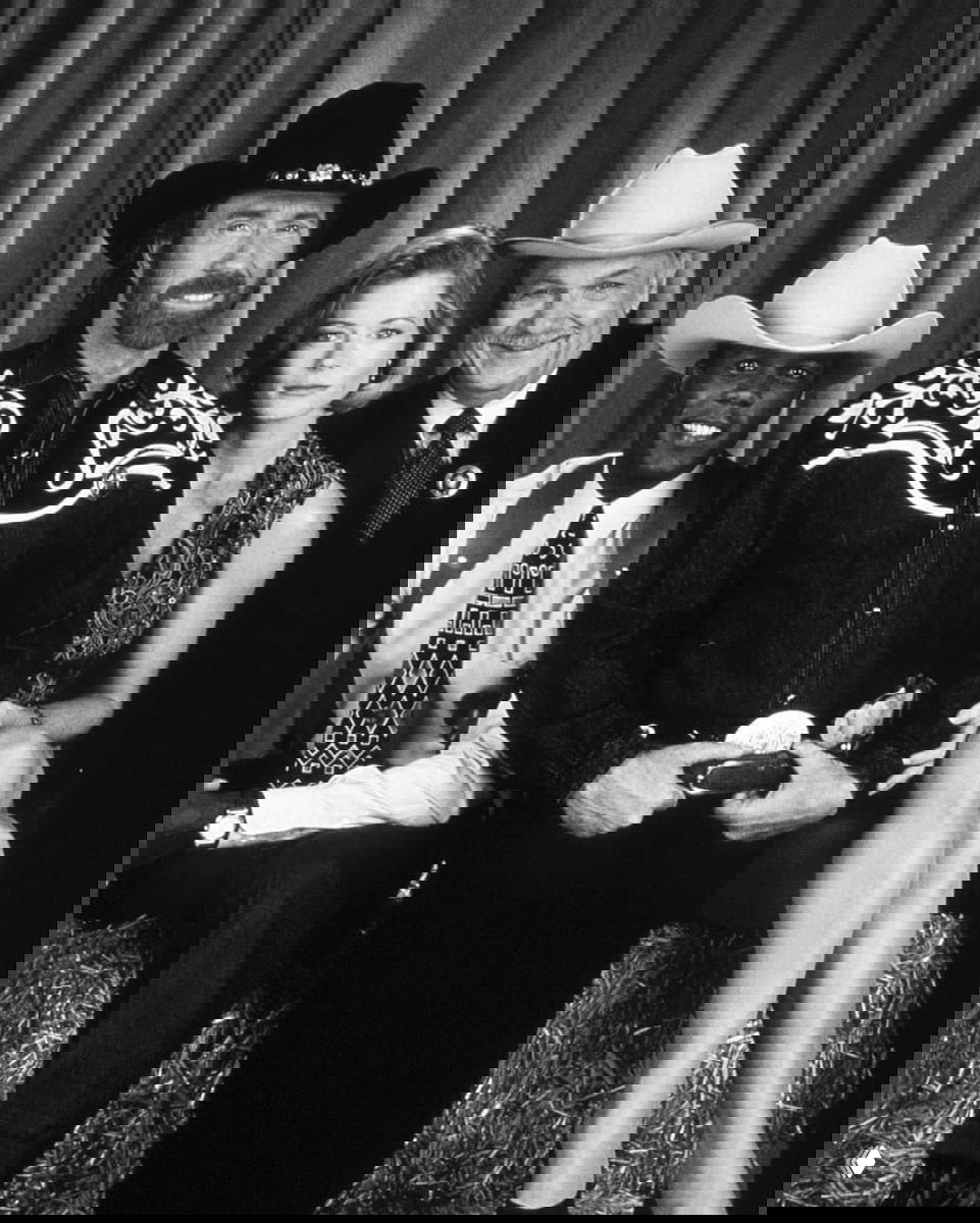 Чёрно-белая групповая фотография: Чак Норрис в ковбойской шляпе в центре, рядом со соактёрами в костюмах вестерна и занавесом на фоне.