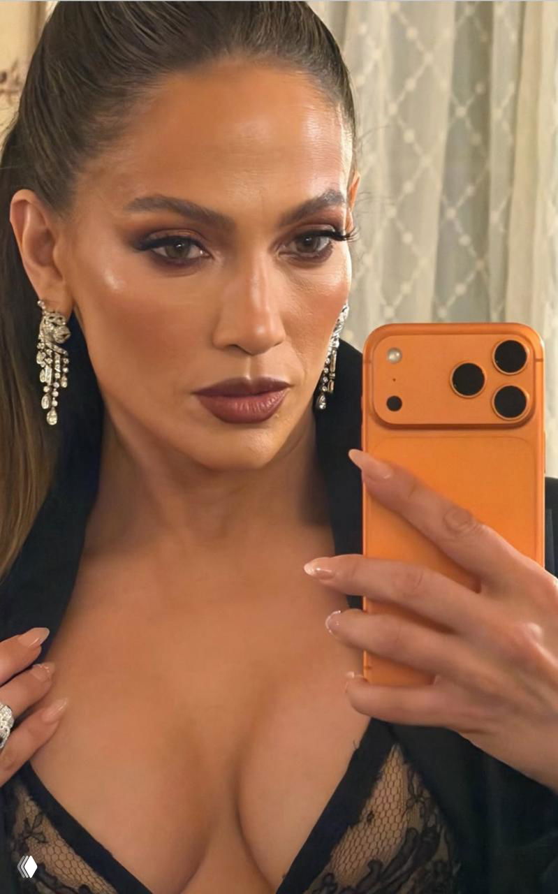 Крупный план женщины с ярким макияжем и серьгами, она делает селфи зеркалом, видно декольте и аксессуары в интерьере.