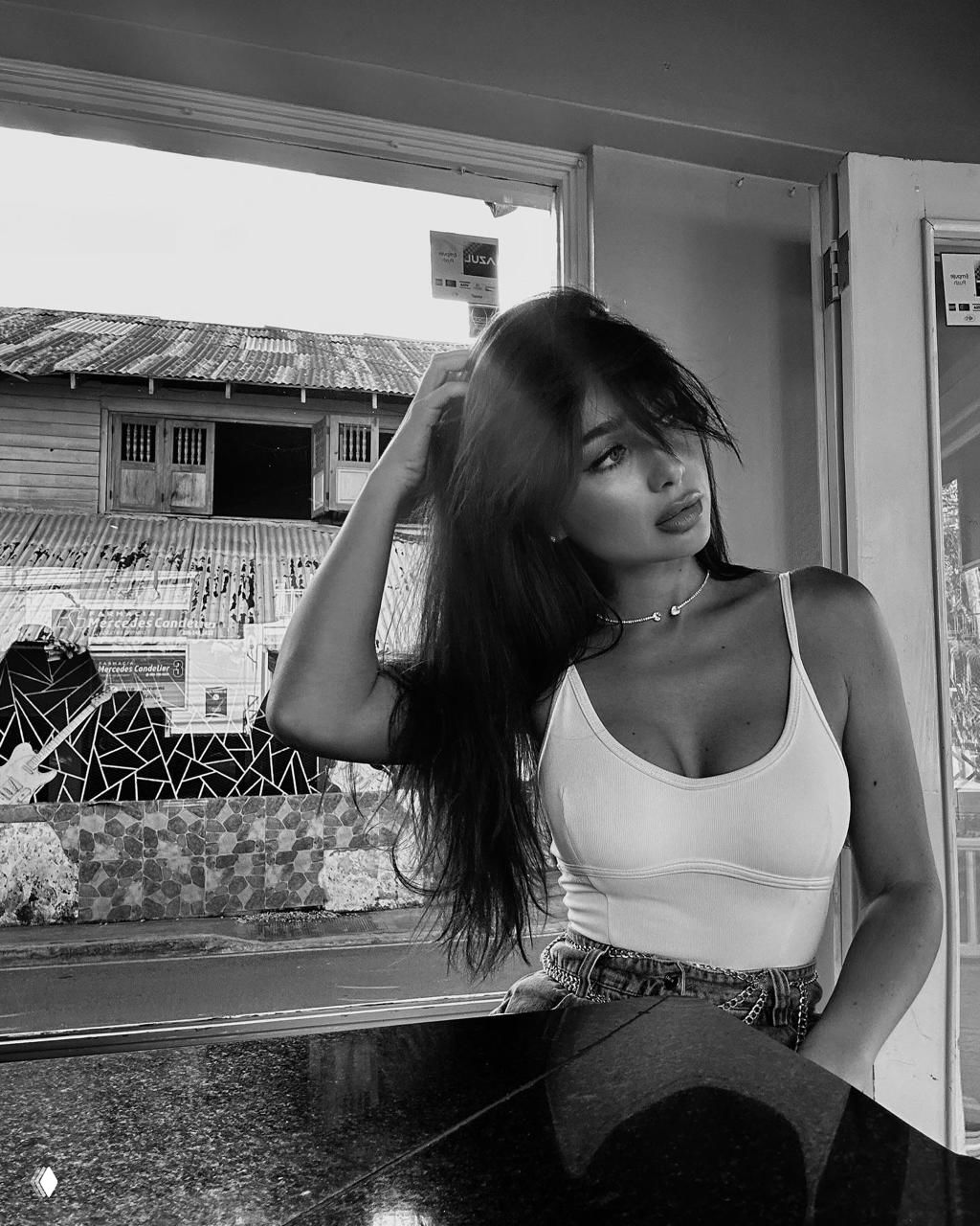 Чёрно-белый портрет женщины в светлом топе в кафе у окна; кадр подчёркивает черты лица и прическу модели.
