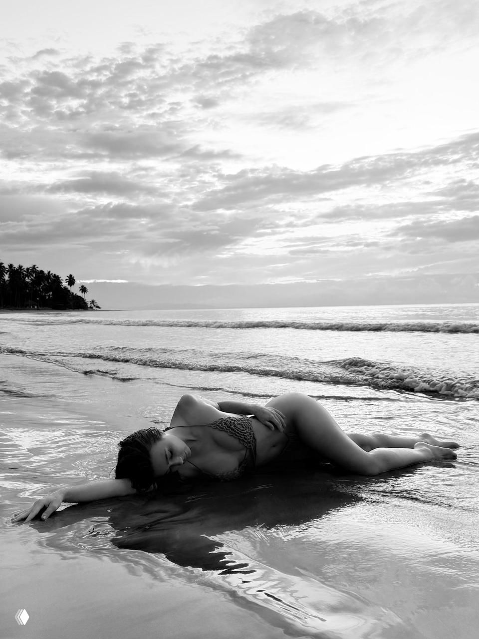 Чёрно-белая фотография женщины в купальнике, позирующей на берегу моря — художественный пляжный кадр с отражением воды.
