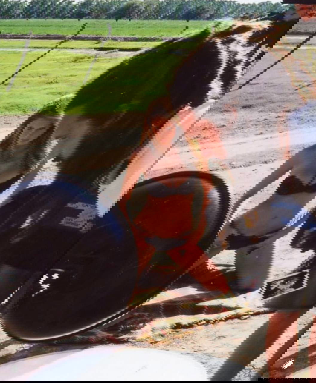 Сцена фотосъёмки на природе: модель в тёмном купальнике, на переднем плане светотехника и операторы, задний план — поле и деревья.