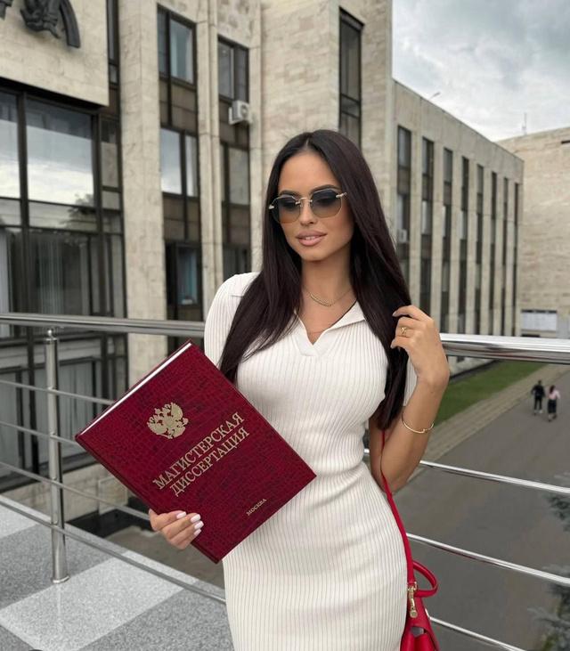 Елизавета Гурьянова в светлом платье держит диплом магистра МГИМО с гербом России на обложке, портретный кадр на балконе университета.