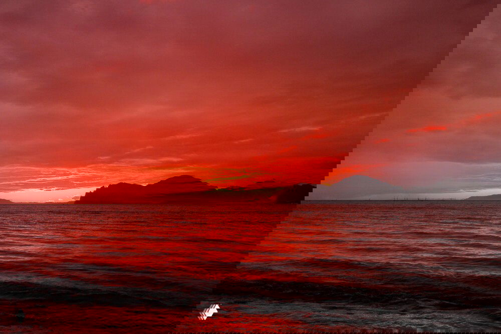 Закат над морем и силуэт гор в Крыму: небо и вода окрашены в тёплые красные оттенки, спокойный прибрежный вид.