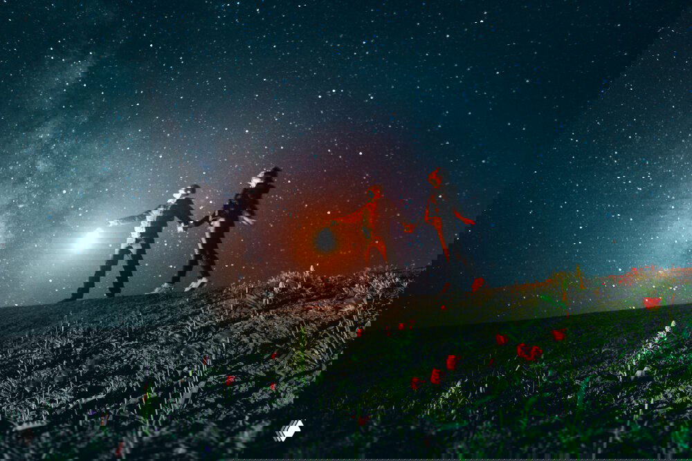 Ночная съёмка: двое людей на холме держат источник света, над ними видна млечный путь — небо и земля в одном кадре.