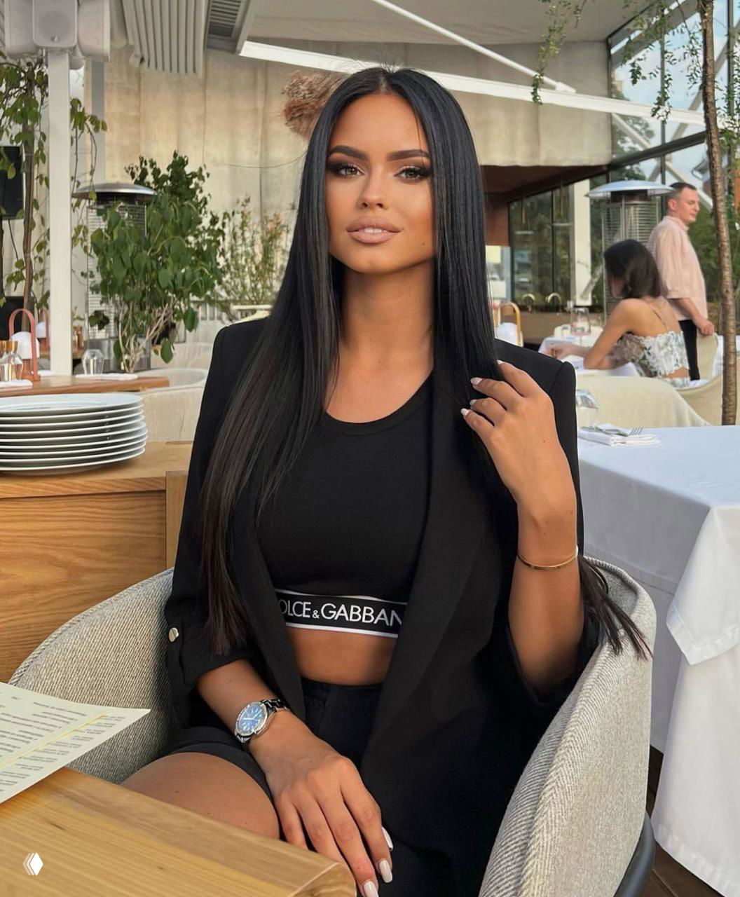 Елизавета Гурьянова в чёрном костюме и кроп‑топе в ресторане, сидит за столом — образ городской моды и вечернего макияжа.