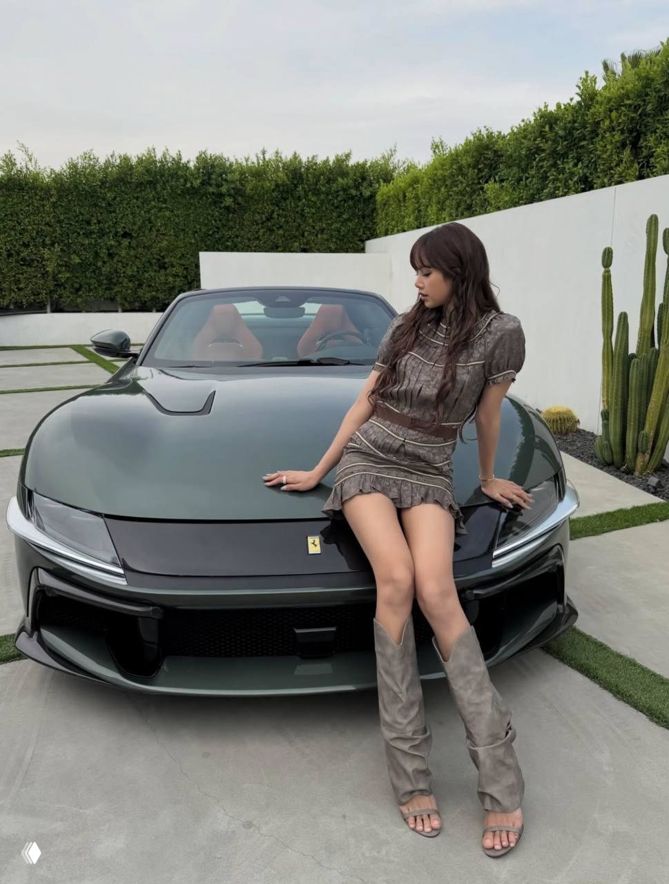 Лиса сидит на капоте зелёного спорткара Ferrari у частного дома в мини‑платье и сапогах; кадр показывает lifestyle-сторону жизни артиста рядом с автомобилем класса люкс.