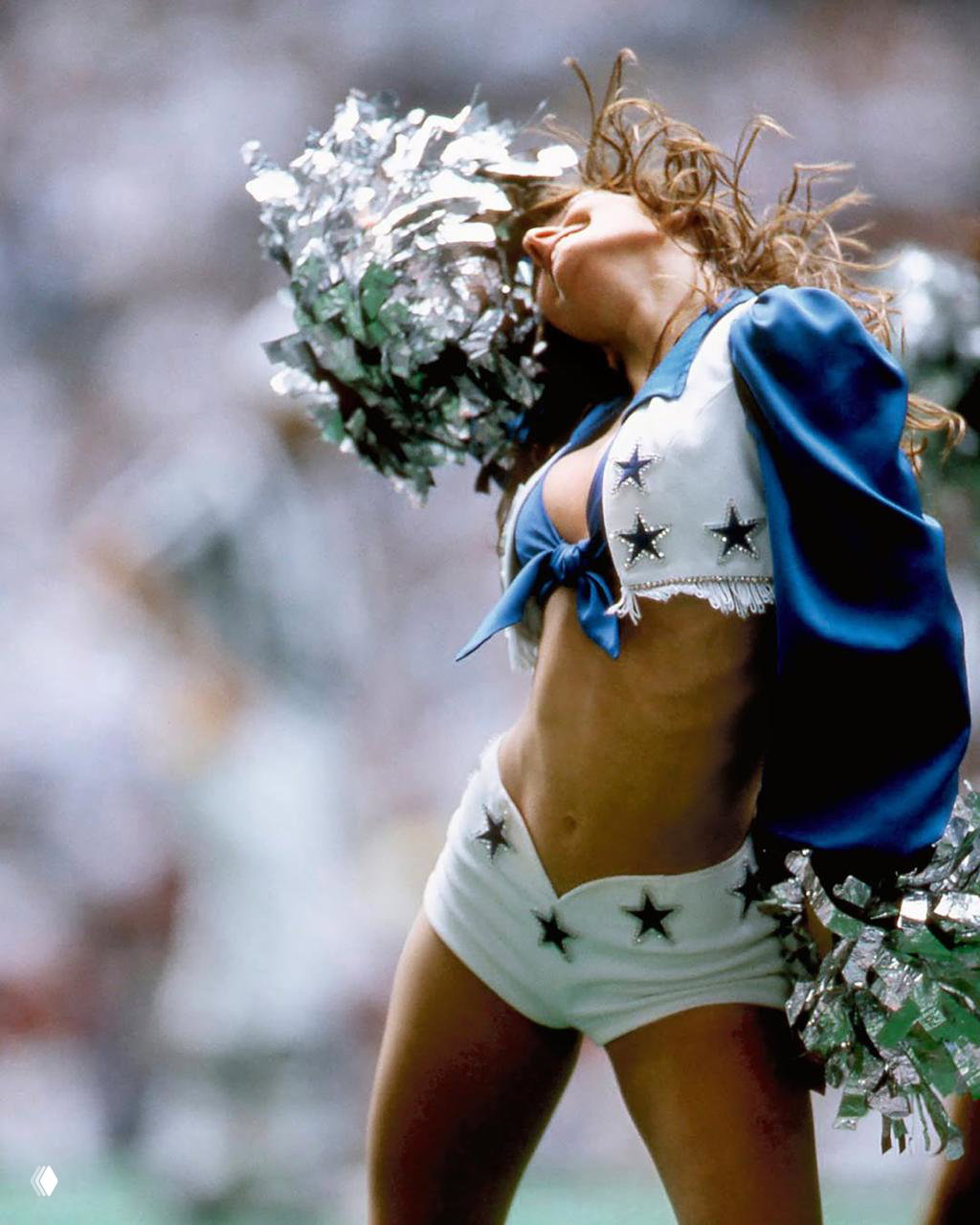 Чирлидерша Dallas Cowboys в характерном костюме со звёздами и помпоном, динамичный кадр в момент движения на матче.
