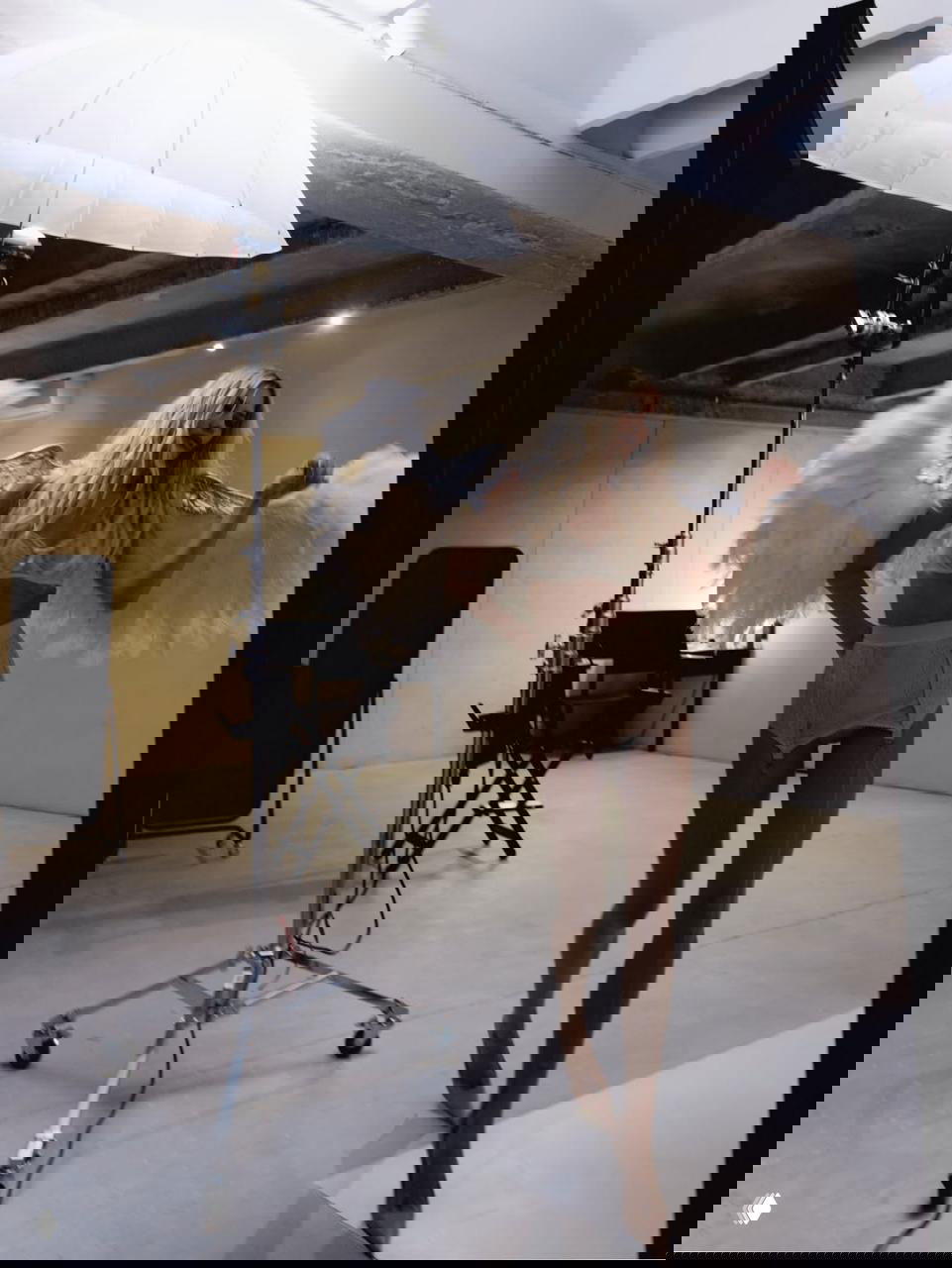 Елена Перминова в корсете и чулках под студийным светом, с крыльями — кадр полного роста, видны софиты и техника съёмки.