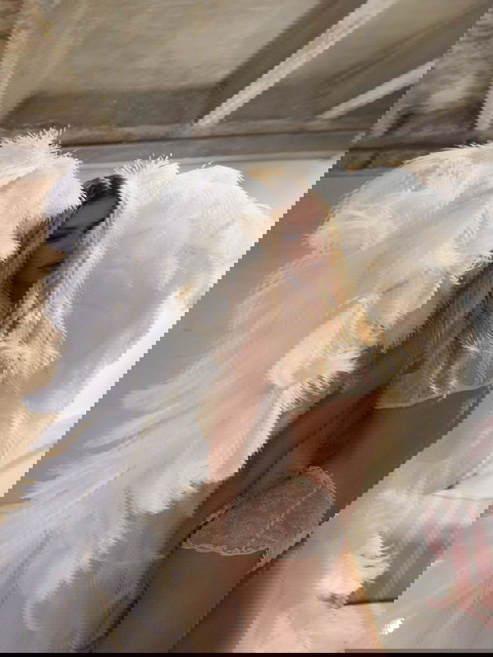 Крупный портрет Елены Перминовой в кружевном белье и пушистых белых крыльях, мягкое освещение и гримерная зона на заднем плане.