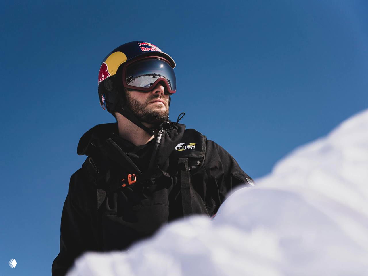 Мужчина в шлеме и горнолыжных очках на снежном склоне: Егор Посохин в экипировке, на переднем плане видна часть параплана и небо.