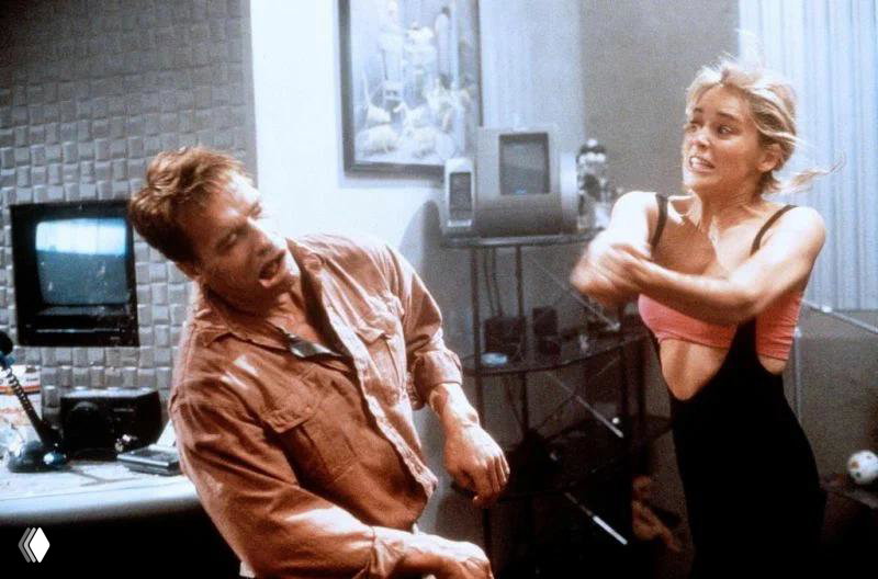 Кадр с двумя персонажами в комнате офиса: женщина в спортивной позе общается с мужчиной, интерьер служебного помещения.