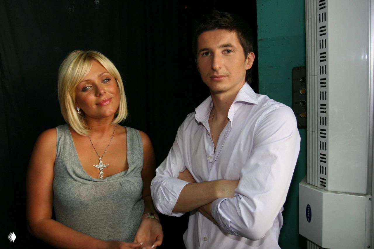 Фотография мужчины в светлой рубашке рядом со светловолосой женщиной на фоне закулисной сцены, архивный снимок в контексте новости.