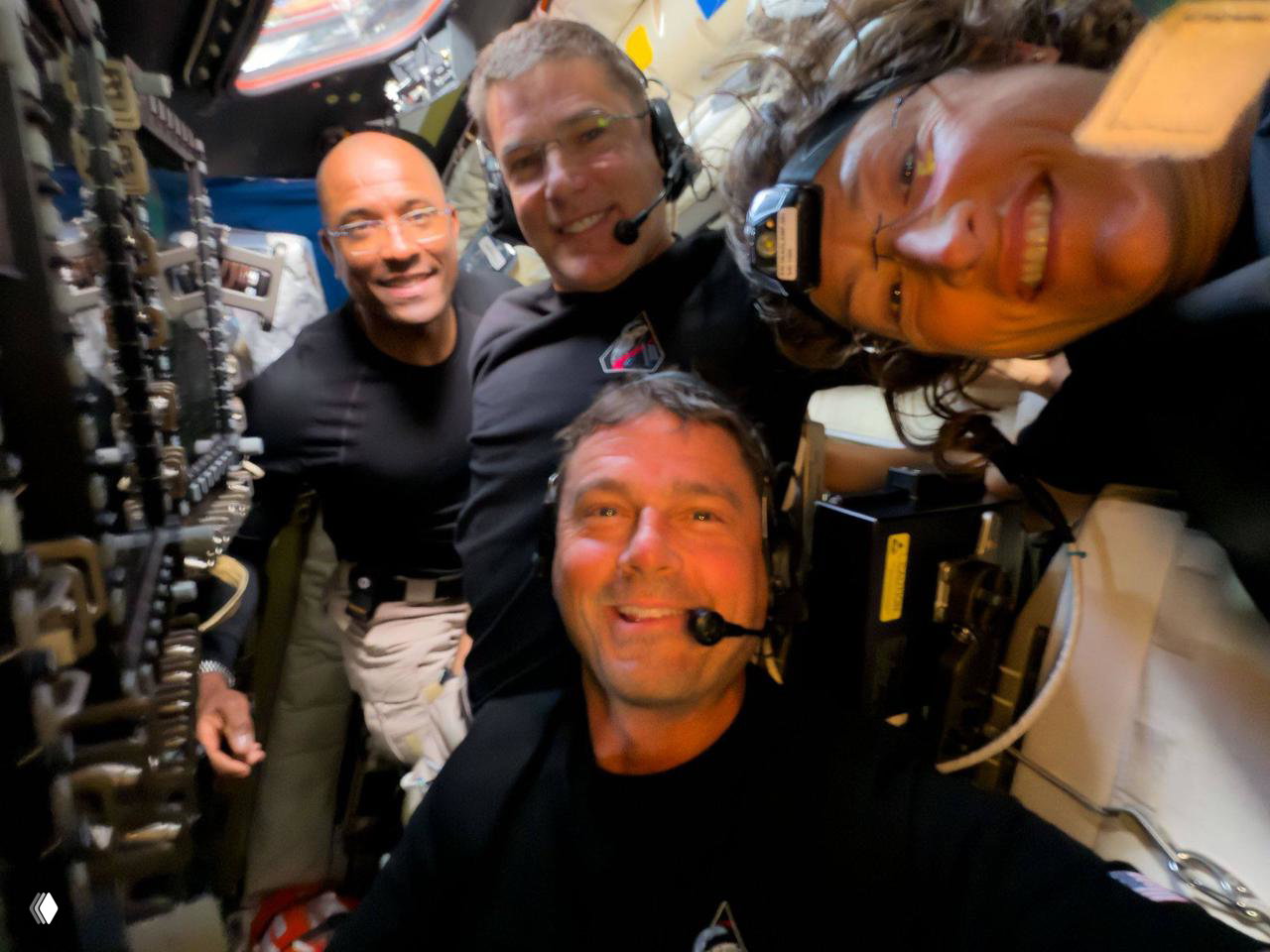 Групповое селфи экипажа миссии «Артемида‑2» внутри модуля: улыбающиеся астронавты в наушниках и с микрофонами, неформальный кадр с элементами интерьера корабля.