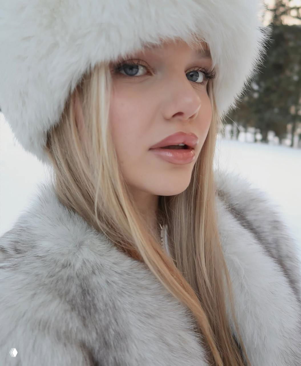 Крупный план молодой женщины в светлой меховой шапке и шубе на снежном фоне, акцент на губы и холодный взгляд в стиле тренда.