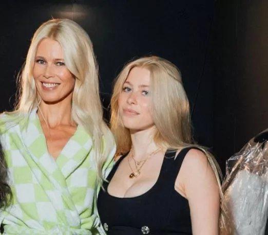 Две женщины на фоне затемнённой сцены: фотография в стиле папарацци с вечернего мероприятия, видны улыбки и светлые волосы