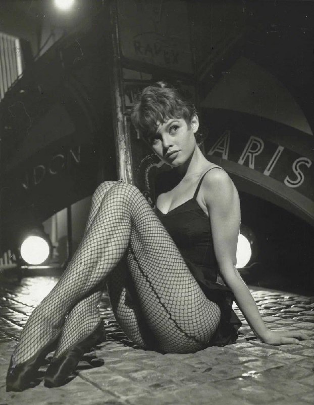 Чёрно-белая фотография молодой Бриджит Бардо в театральном образе с сетчатыми чулками, кадр из фотосессии на съёмочной площадке.