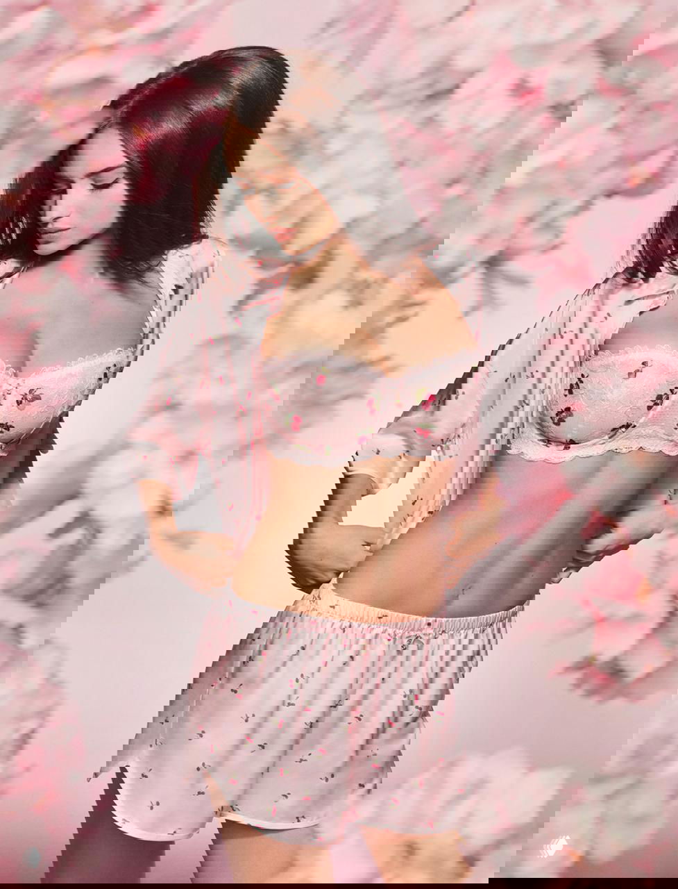 Фотография модели в розовом комплекте нижнего белья и шёлковой рубашке на фоне розовых цветов, рекламный образ, студийное освещение.