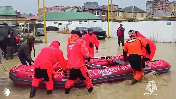 Группа спасателей в ярких оранжевых костюмах готовит надувную лодку к спуску в воду при массовой эвакуации пострадавших от наводнения.