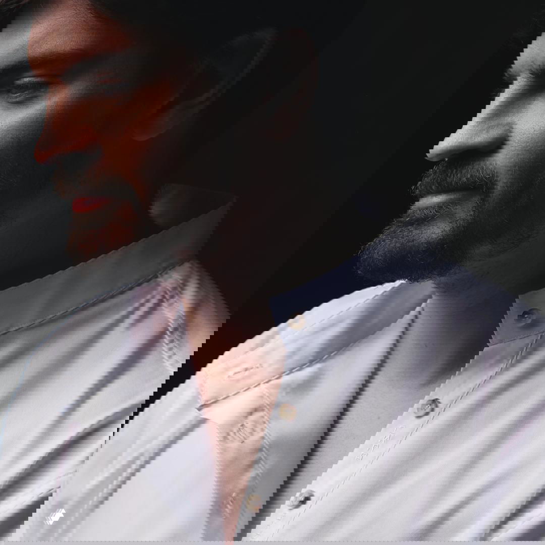 Крупный план профиля мужчины в белой рубашке с отложенным воротником; видна деталь внутренней планки и текстильная вышивка.