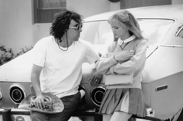 Чёрно‑белый кадр: диалог между членом съёмочной группы и молодой актрисой у автомобиля в гриме и костюме для сцены.