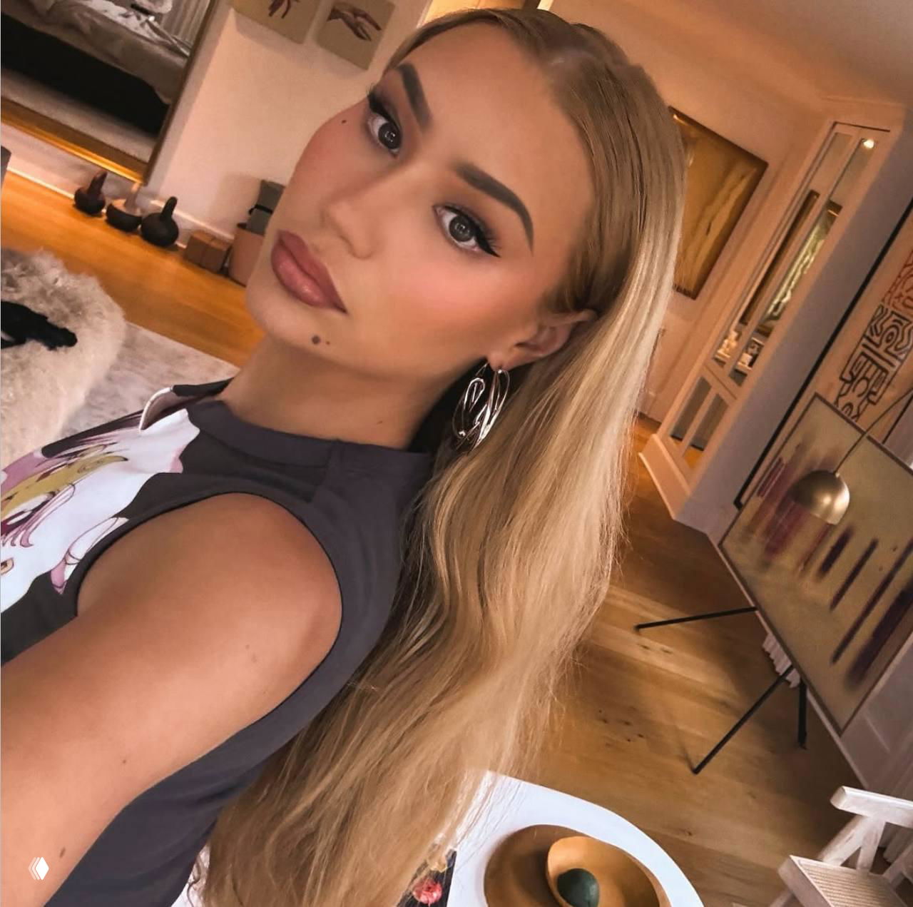 Крупный портрет модели с светлыми волосами и выразительным макияжем, кадр снят в интерьере, акцент на лице и украшениях.